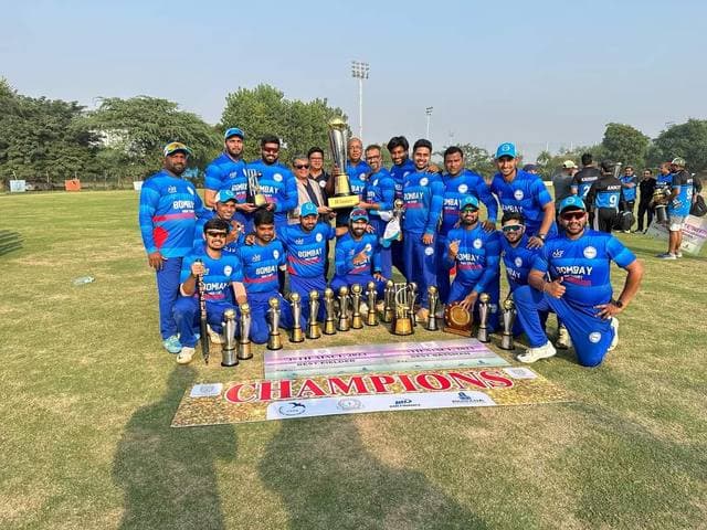 A team in blue kit kneeling behind rows of trophies under a Champions banner