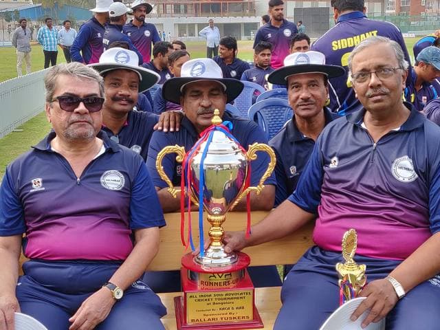 Players in navy and pink shirts seated on a bench behind a gold cup with a Runners-up plate