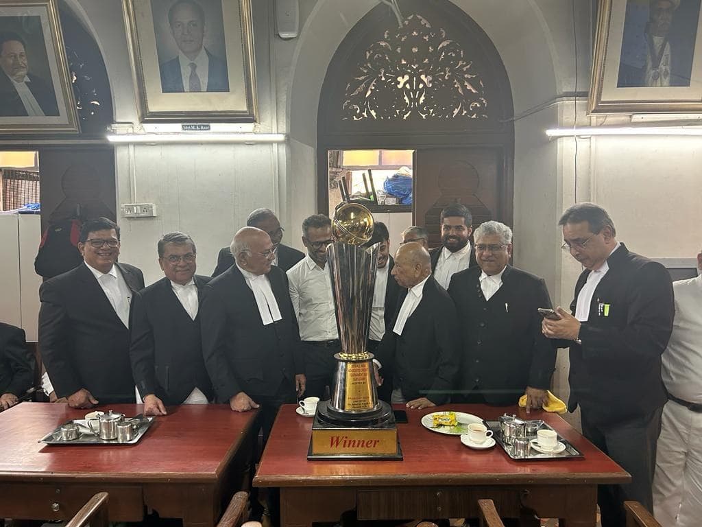 Advocates in black court gowns standing behind a table with a gold cup