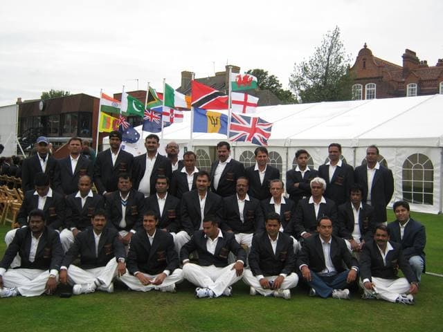 A team in blazers and white trousers in front of flags and a marquee